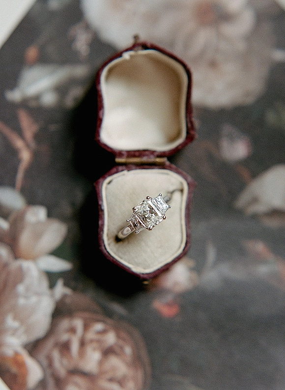 Engagement ring in a ring box with diamond accents, photographed close up on a floral pattern surface for wedding detail flat lay