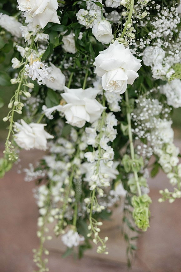 Wedding floral arrangement of white rose wedding flowers with baby's breath and greenery cascading beneath hanging florals on an outdoor walkway