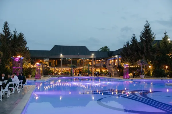 Poolside wedding reception with wedding reception by pool seating, purple uplighting and string lights reflecting on the water at dusk