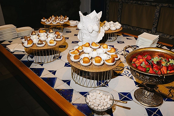 Dessert table wedding dessert bar with mini dessert cups on tiered stands, strawberries and white candy on a blue patterned tile tabletop indoors
