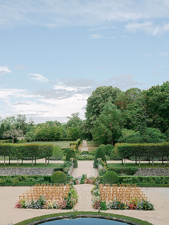 Outdoor ceremony setup with garden wedding ceremony rows of wood chairs and flower-lined aisle in a formal garden by a reflecting pool