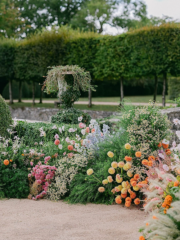 Wedding floral installation with ceremony ground florals in meadow style, featuring daisies, dahlias and greenery along a gravel path by hedges