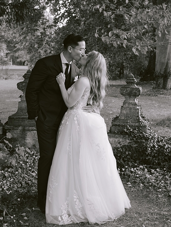 Wedding kiss portrait of bride and groom kissing, her strapless lace dress and tulle skirt against an ivy stone wall in a garden