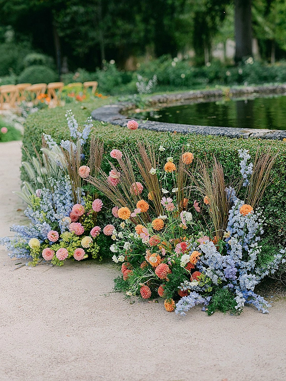 Ceremony aisle florals with wedding aisle ground flowers in pastel blooms and dried grasses bordering a stone garden walkway by a pond