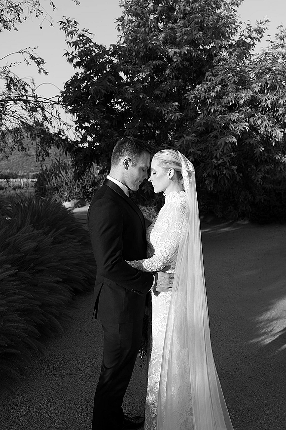 Couple portrait in black and white wedding portrait style, bride and groom embrace with forehead touch on a garden path, veil flowing