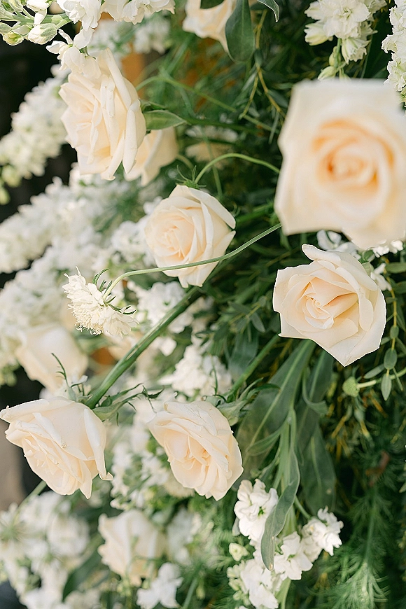 Wedding floral arrangement of ivory rose wedding flowers with lush greenery, captured in a close up against soft, blurred florals background