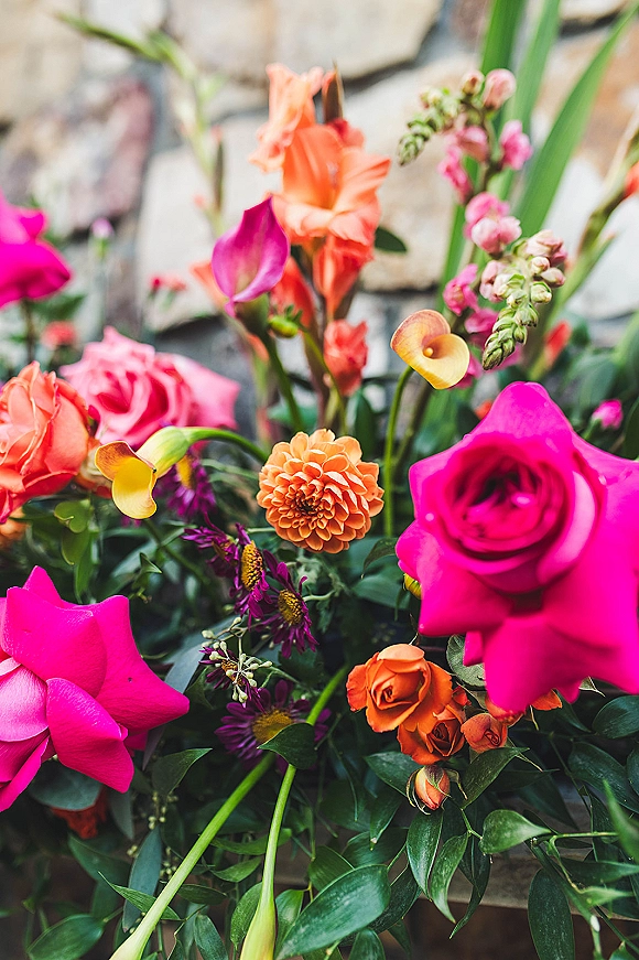 Wedding flowers in a hot pink rose bouquet with orange roses and dahlia, set against a textured stone wall backdrop