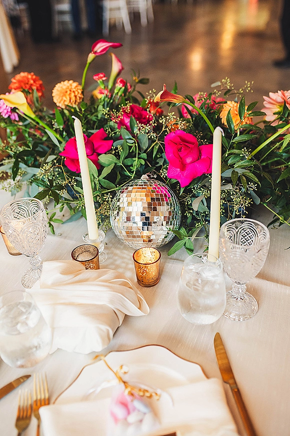 Reception tablescape with wedding table centerpiece of hot pink roses, calla lilies, and greenery, plus taper candles and crystal goblets on wood floor