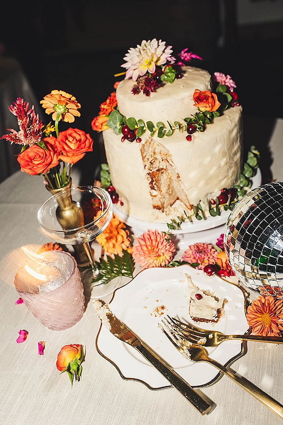 Wedding cake with textured buttercream, topped with orange roses and pink flowers, beside a plated slice, gold flatware and disco ball decor
