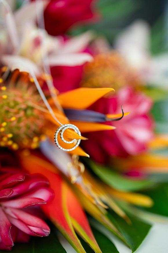 Wedding rings nestled in tropical flowers and greenery leaves, diamond bands sparkling against a softly blurred floral arrangement background