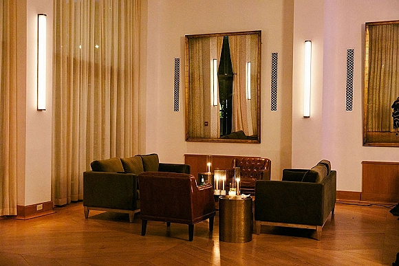 Lounge seating area with wedding lounge seating, sofas and leather chairs around a round table with pillar candle clusters on wood floors