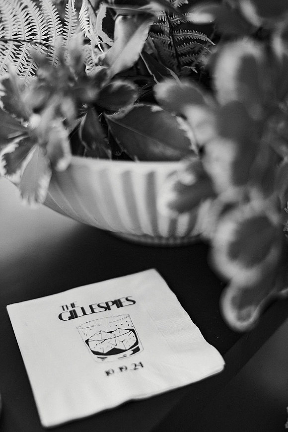 Wedding cocktail napkin with custom cocktail napkins monogram and cocktail illustration beside a potted fern on a tabletop