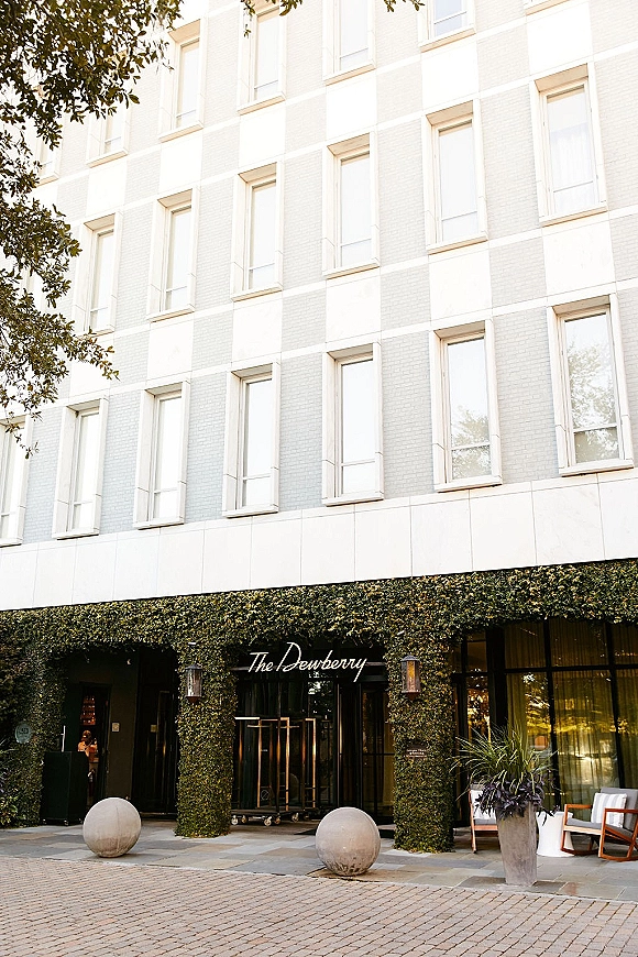Wedding venue exterior with ivy-covered facade and venue signage, glass entrance doors framed by wall lanterns and patio seating on the sidewalk