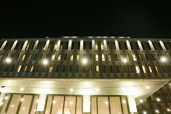 Wedding string lights draped as bistro lights wedding canopy against a modern building facade, glowing warm white under the night sky