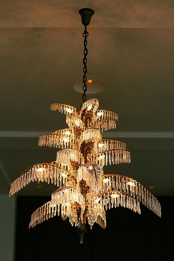 Wedding chandelier with crystal chandelier wedding details, cascading crystals and warm bulbs hanging by chain from a reception room ceiling