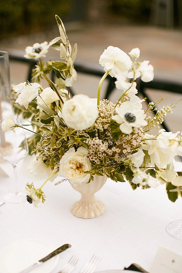 Wedding centerpiece with a white floral centerpiece and greenery in a ceramic pedestal vase on a white tablecloth in an indoor dining space