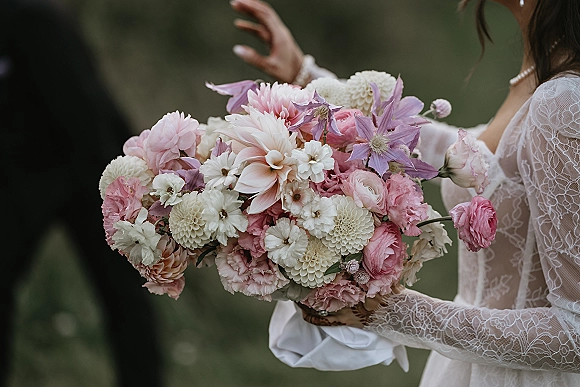 Bridal bouquet of pastel wedding bouquet blooms with dahlias, ranunculus and clematis, wrapped in ribbon against blurred greenery background