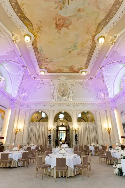 Ballroom reception decor in a round table reception layout beneath a ceiling fresco, framed by ornate molding and arched doorways.