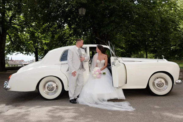 Couple portrait and wedding car photo, the bride and groom standing beside a classic car, sharing a candid look together.