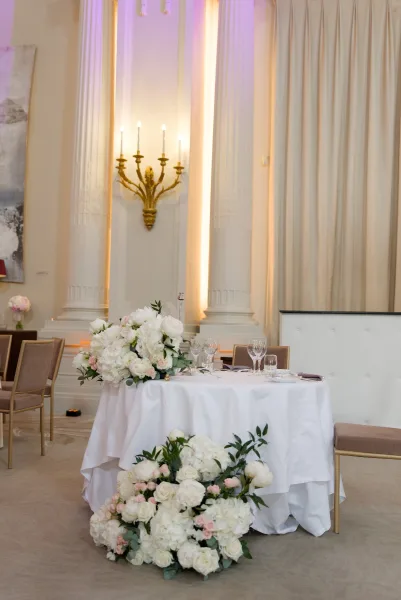 Sweetheart table styled for ballroom reception decor, adorned with white and blush florals, set before ballroom columns and soft drapery.