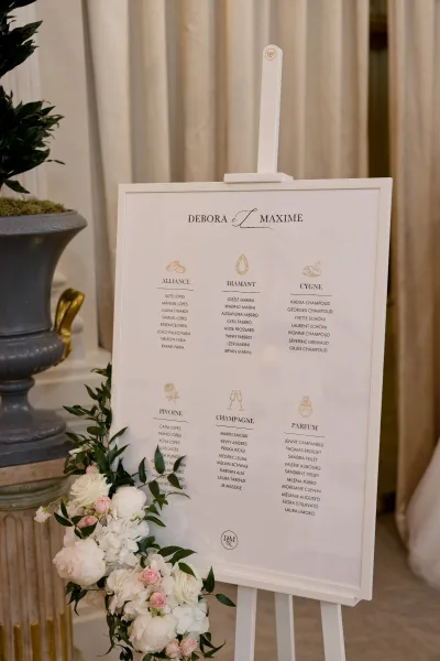 Wedding seating chart with florals set against draped curtains, with an urn planter on a pedestal completing the elegant display.