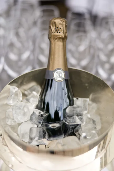 Champagne bottle chilled, champagne on ice, with a row of champagne flutes softly blurred in the background.