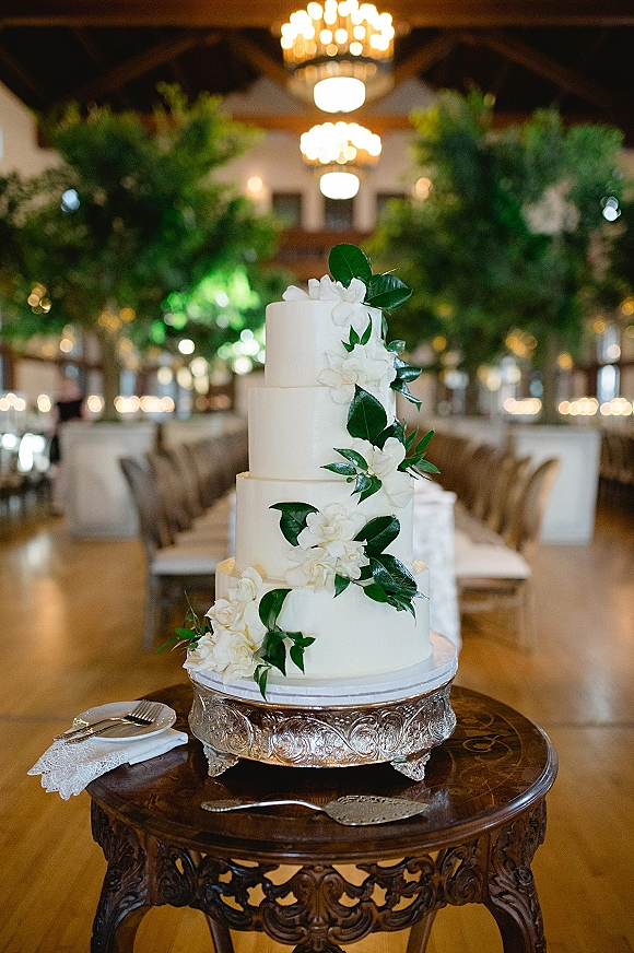 Wedding cake tiered wedding cake with sugar flowers and greenery on a stand, set on a wooden table under chandeliers in a reception hall