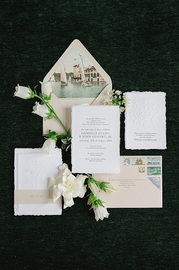 Invitation suite with deckled edge wedding invitations, embossed monogram and stamped envelope, styled on dark fabric with white florals