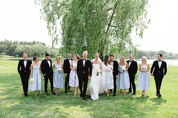 Wedding party portrait with bride and groom with wedding party, bride in strapless dress and long veil holding bouquets on a lakeside lawn