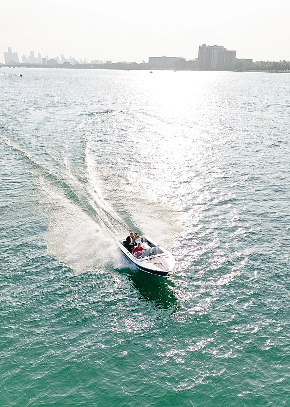 Couple boat ride on a speedboat, leaving a bright wake across sunlit open water with hazy city skyline in the distance