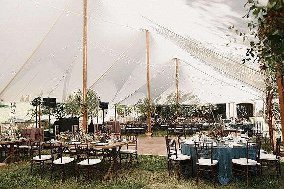 Tent reception decor under a sailcloth wedding tent with string lights, mixed tables, floral centerpieces, candles, and dance floor on a lawn by trees