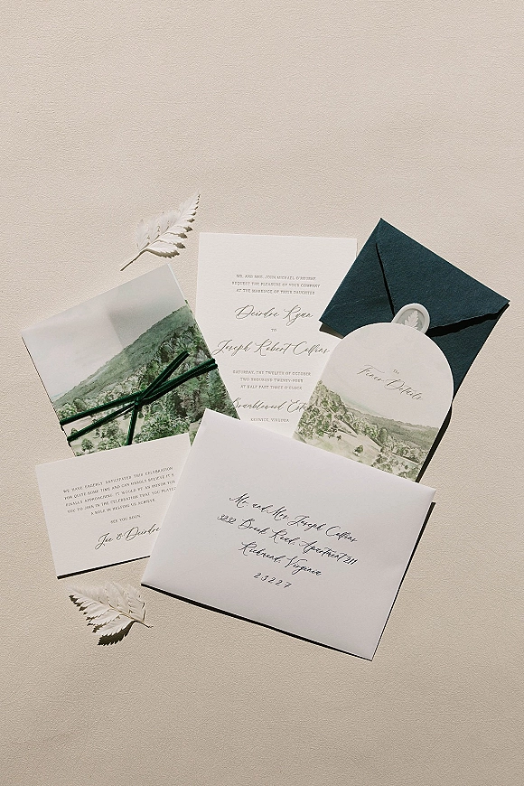 Invitation suite wedding invitation set laid on textured paper, featuring illustrated card, vellum wrap, dark green ribbon, and white wax seal envelopes