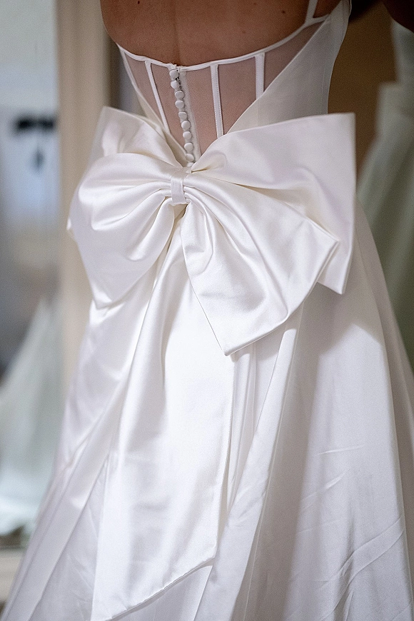 Wedding dress back with an oversized satin bow, corset lacing and button details flowing into a tulle skirt in a neutral indoor room
