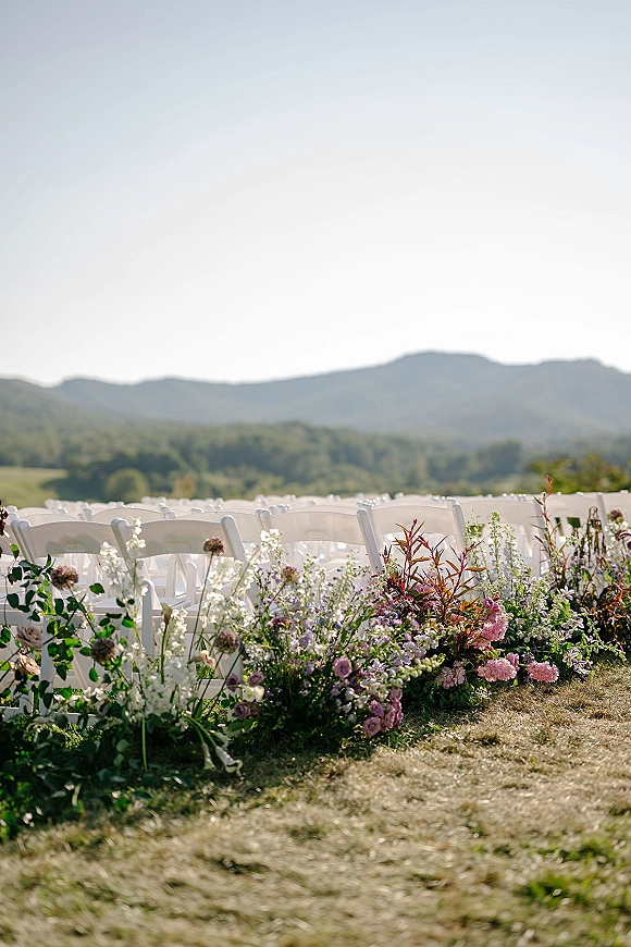 Ceremony seating with outdoor wedding ceremony chairs, rows of white folding chairs lined by wildflower aisle flowers in a mountain field