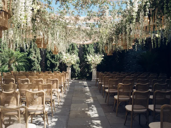 ceremony setup featuring garden ceremony decor with woven pendant lights over a stone patio framed by a brick wall and evergreen trees