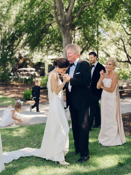 Father daughter dance, a tender wedding reception dance moment on a garden lawn, bride's long train trailing as they sway on the walkway.