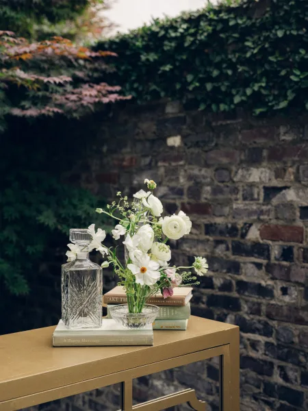 Wedding decor reception vignette on a gold console table styled with delicate pieces, set before an ivy-clad brick wall and garden foliage.