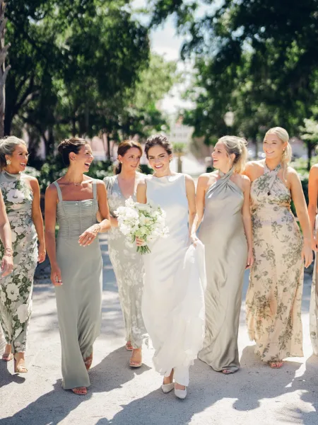 Bridal party portrait of the bride with bridesmaids on a sunlit tree-lined path, the bride holding a white bridal bouquet.
