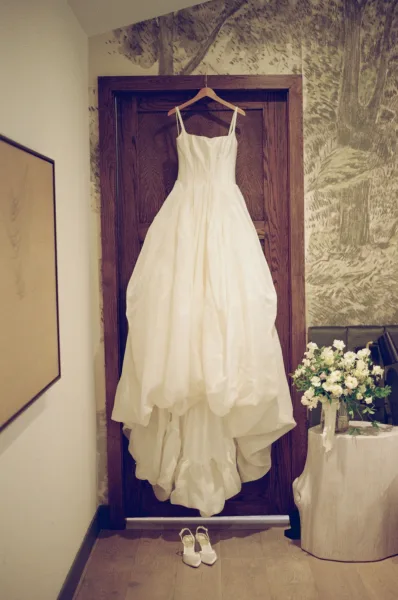 Wedding dress, a bridal gown hanging on a wooden door, with wedding shoes set below and a subtle wallpaper mural adding vintage charm.