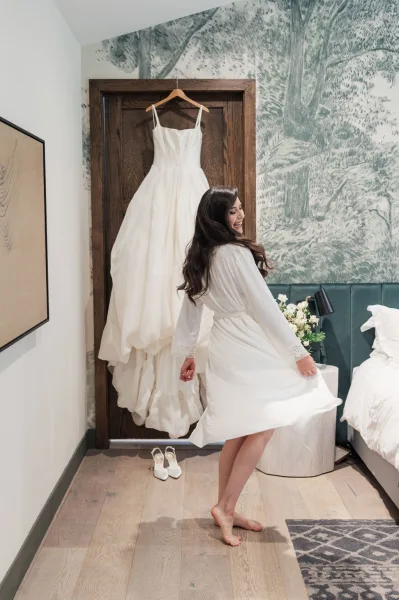 Bride getting ready in a robe beside a wallpaper mural in a cozy bedroom with hardwood floors and an area rug.