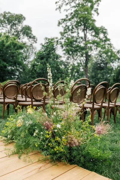 Ceremony aisle decor for a garden ceremony setup, with green-and-white florals edging the aisle and rows of classic bentwood chairs.