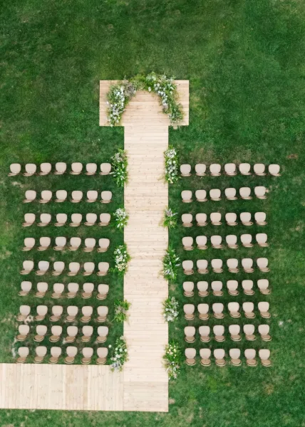 Ceremony setup for an outdoor wedding ceremony featuring a wooden aisle on a grass lawn, flanked by symmetrical seating.
