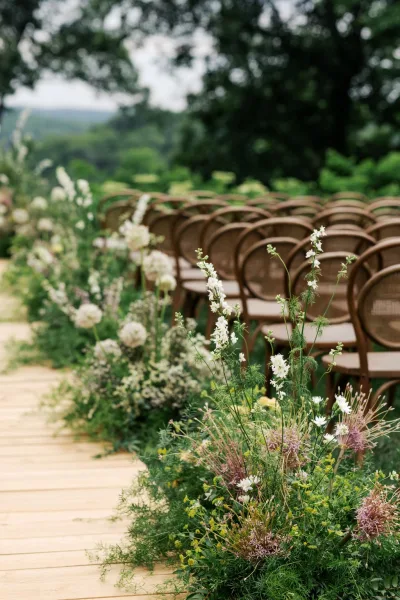 Ceremony aisle design for an outdoor ceremony setup with a wooden walkway, framed by garden trees and distant hills under an open sky.