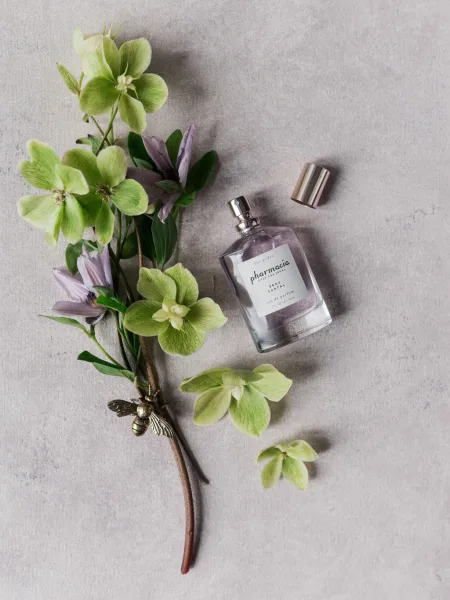 Wedding perfume bottle styled in a delicate perfume flatlay with a gold bee charm on a textured gray surface.