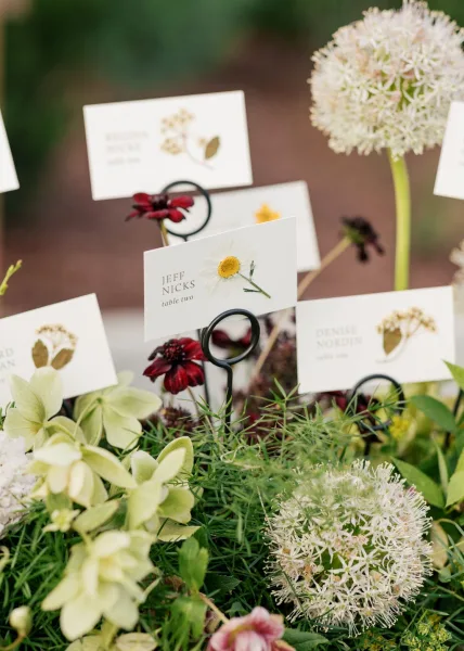 Escort card display of wedding escort cards arranged in neat rows on metal card holders amid garden plants and soil.