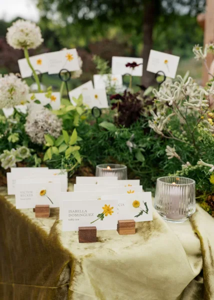 Escort card display on a garden escort card table, set on a rich velvet tablecloth amid garden trees.