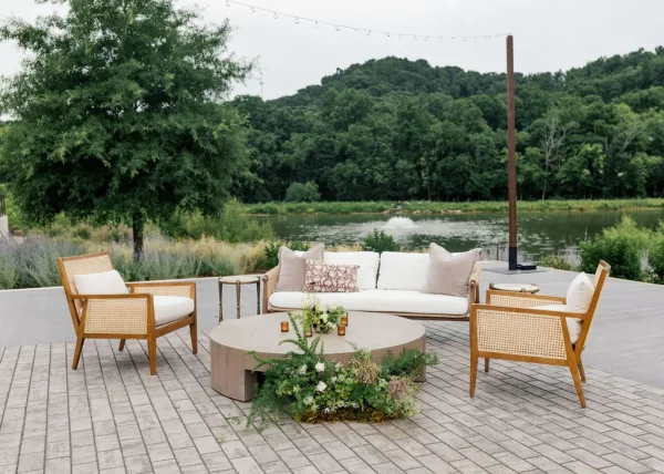 Wedding lounge styled as a cozy reception lounge area with cane lounge chairs set on patio pavers beside a tranquil lake and hills