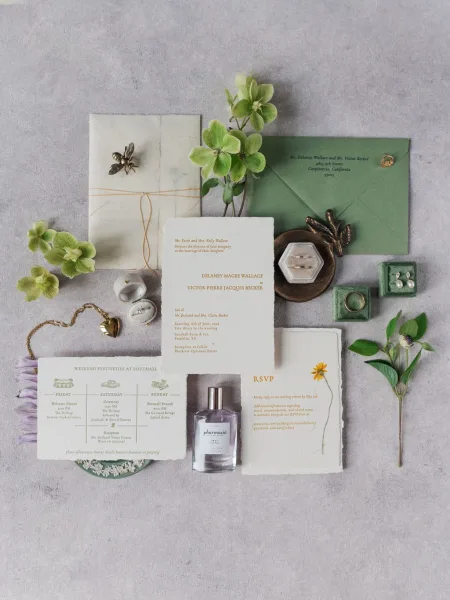 Wedding invitation suite with botanical wedding invitations styled with green florals on a gray textured surface.