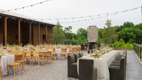 Outdoor reception setup for an al fresco wedding reception under string lights beside a wooden barn.