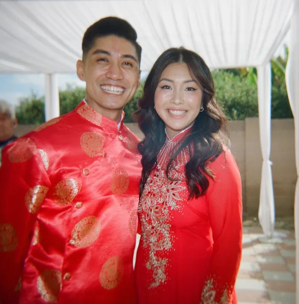 Couple portrait of a wedding couple smiling in red and gold traditional wedding attire under a white canopy tent by greenery